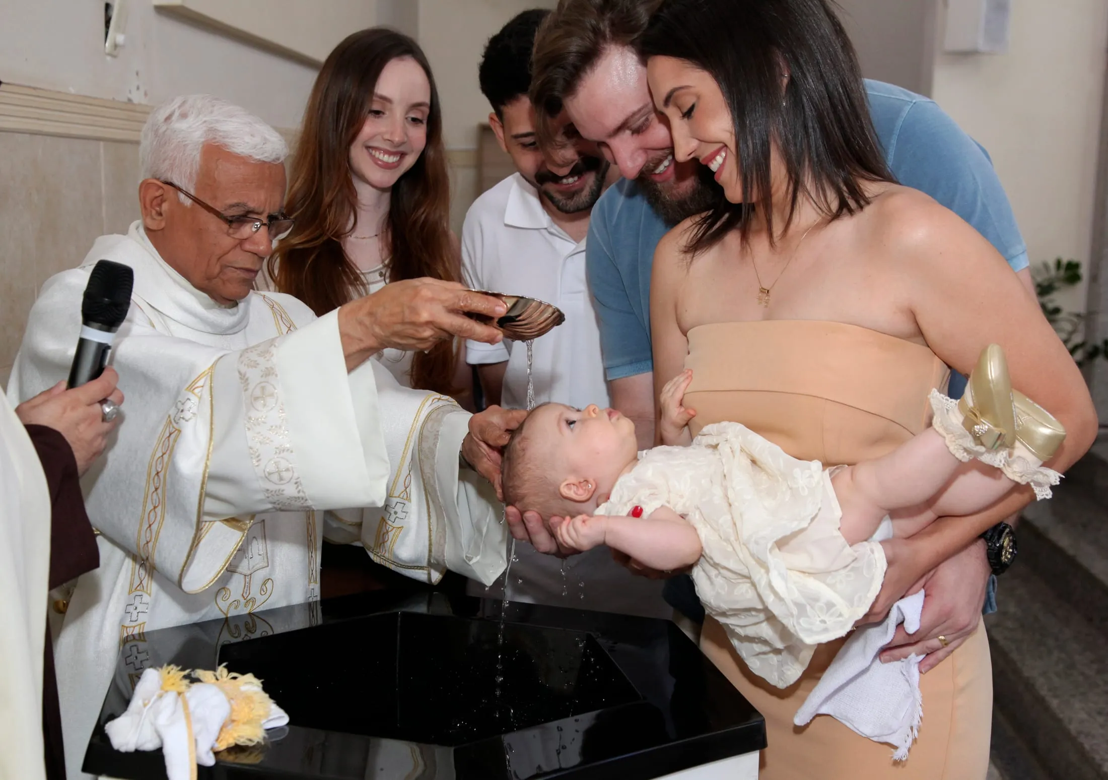 Fotografia de batismo em Piracicaba — padre derramando a água com a comunidade ao redor